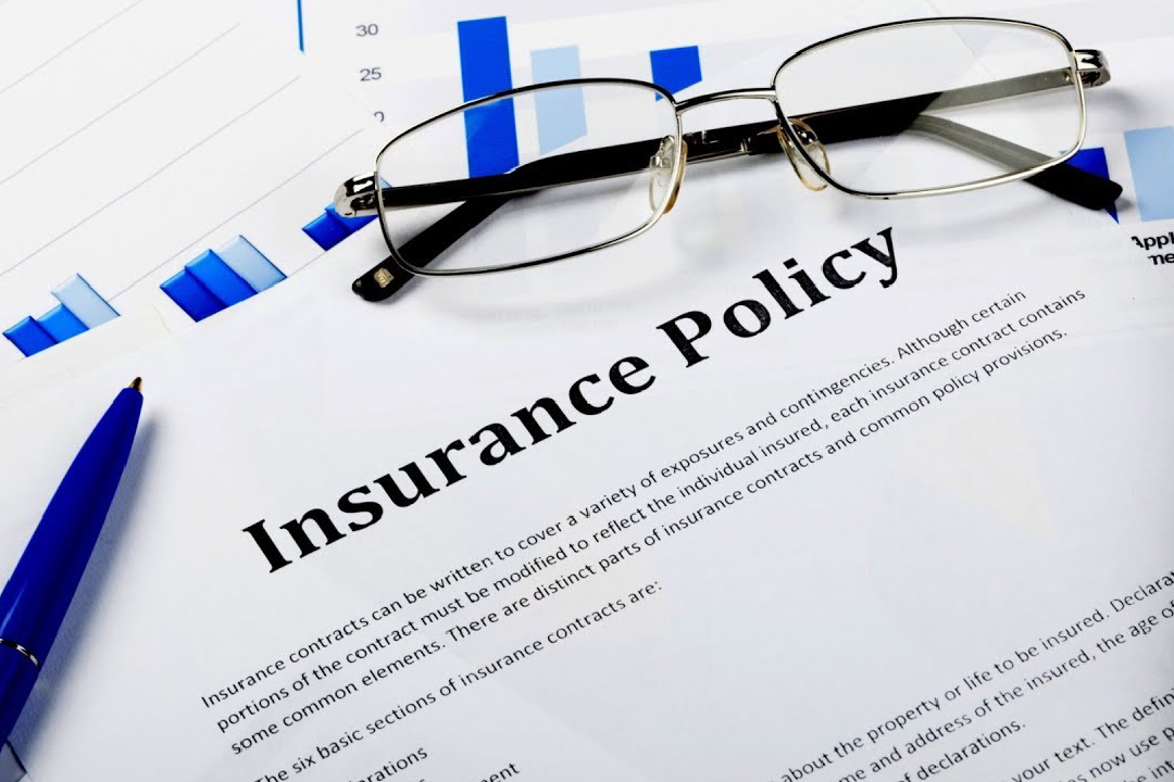 closeup of insurance policy paperwork with eyeglasses and pen